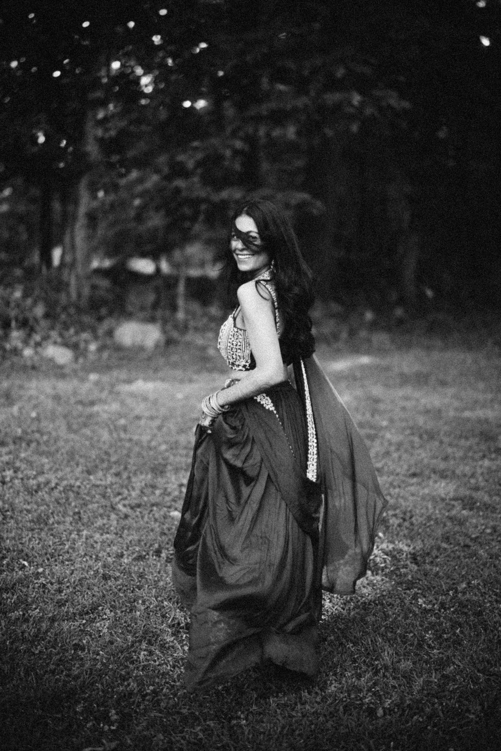A black and white portrait of a woman in a flowing vintage dress with a masquerade mask standing in a garden setting.  Hilton Pearl River NY