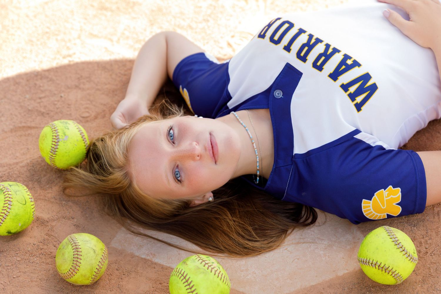 Portrait of softball player lying on ground surrounded by yellow softballs.