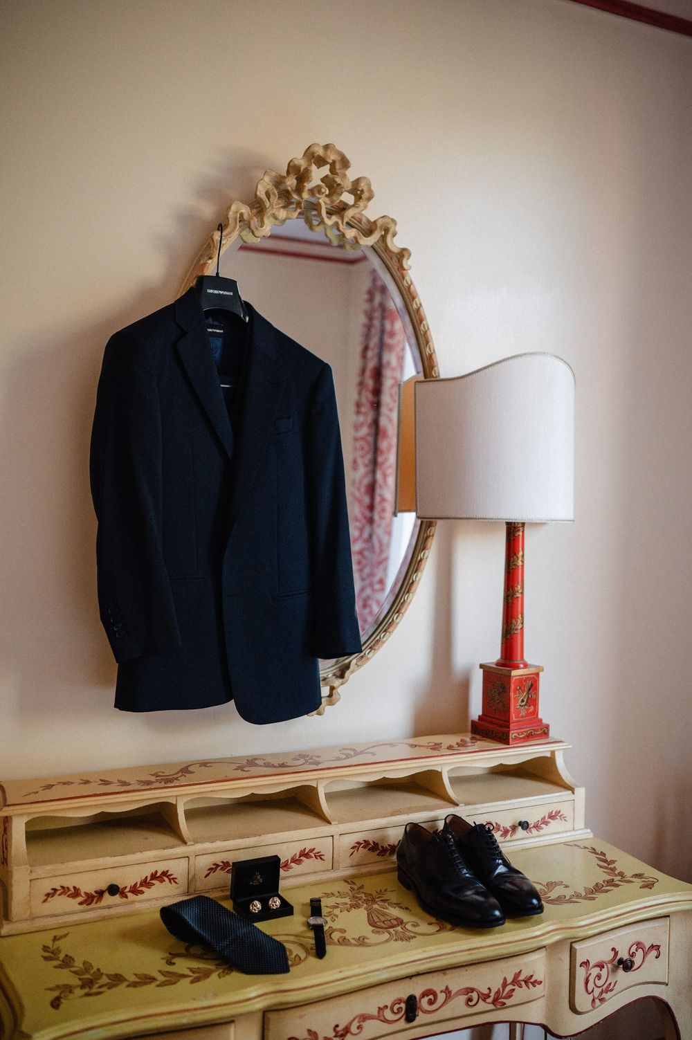 Black formal suit and dress shoes displayed on a vintage cream-colored dresser with decorative floral patterns.