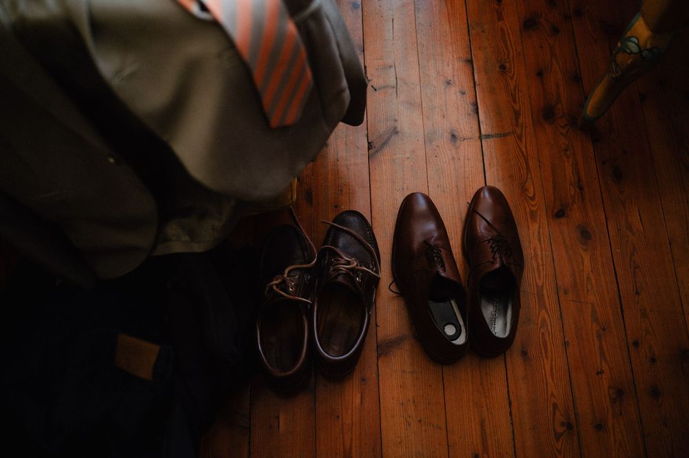 Stylish leather shoes and sneakers lined up on a distressed wooden floor in warm lighting.