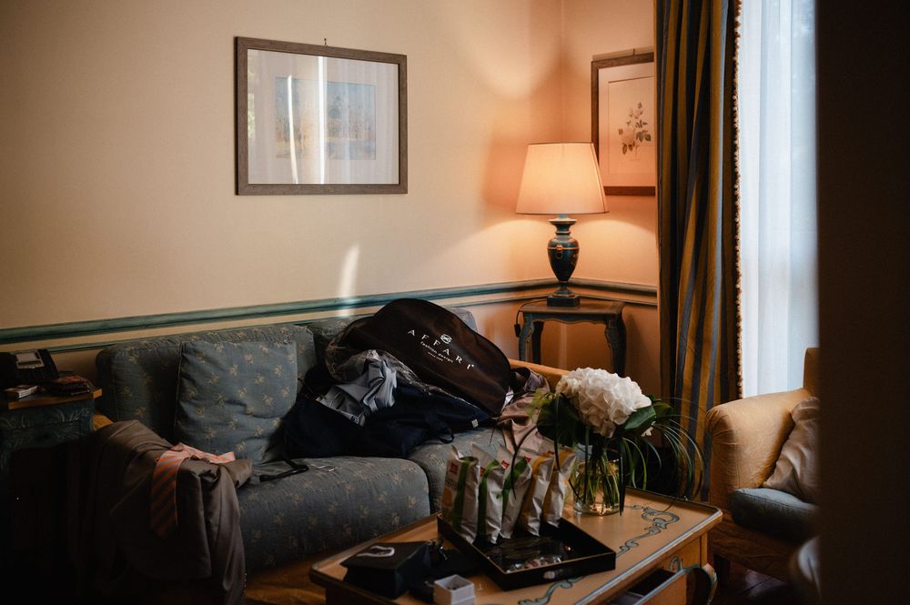 Cozy living room corner with gray sofa, table lamp, and curtained window in warm ambient lighting.