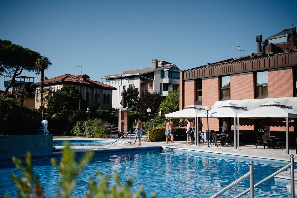 Resort swimming pool with blue water surrounded by modern buildings and lush landscaping in a Mediterranean setting.
