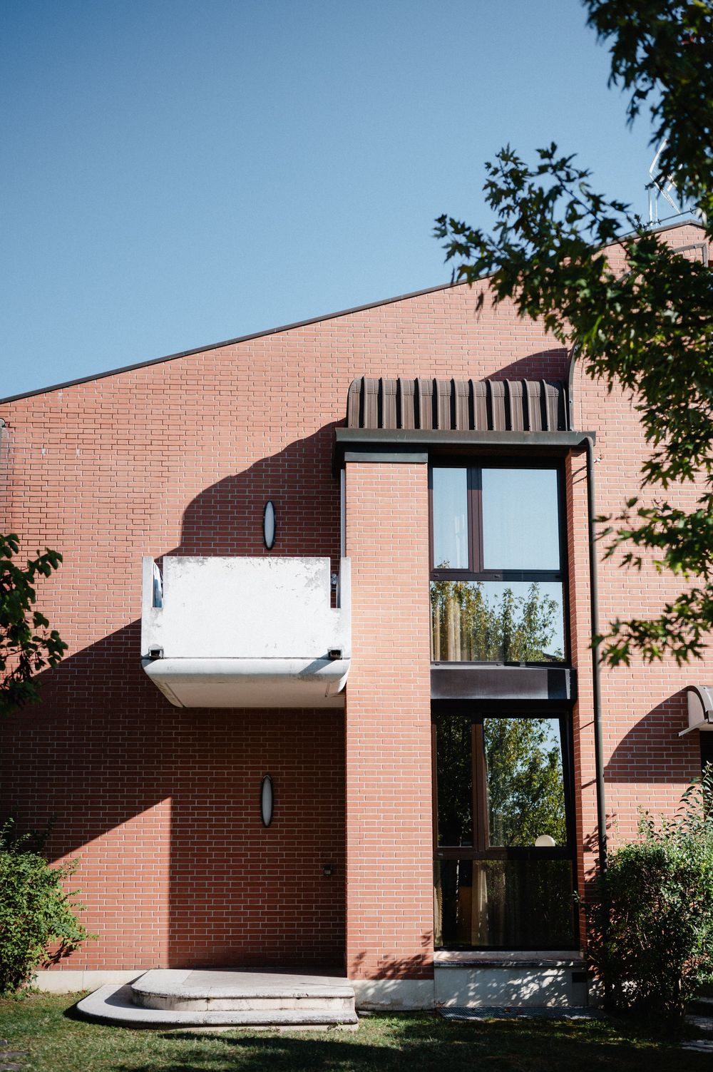 Modern brick house exterior features tall glass windows with black frames against a salmon-colored facade and trees.