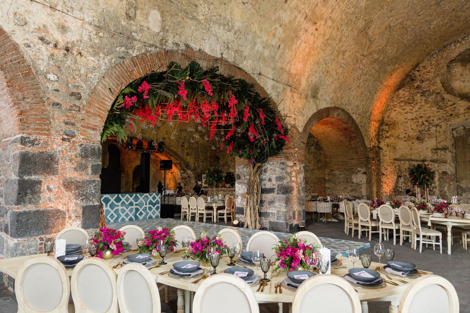 Stone archway wedding venue decorated with elegant floral arrangements and white chairs.