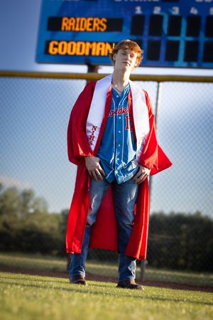 Person wearing bright red coat and denim overalls stands on baseball field.