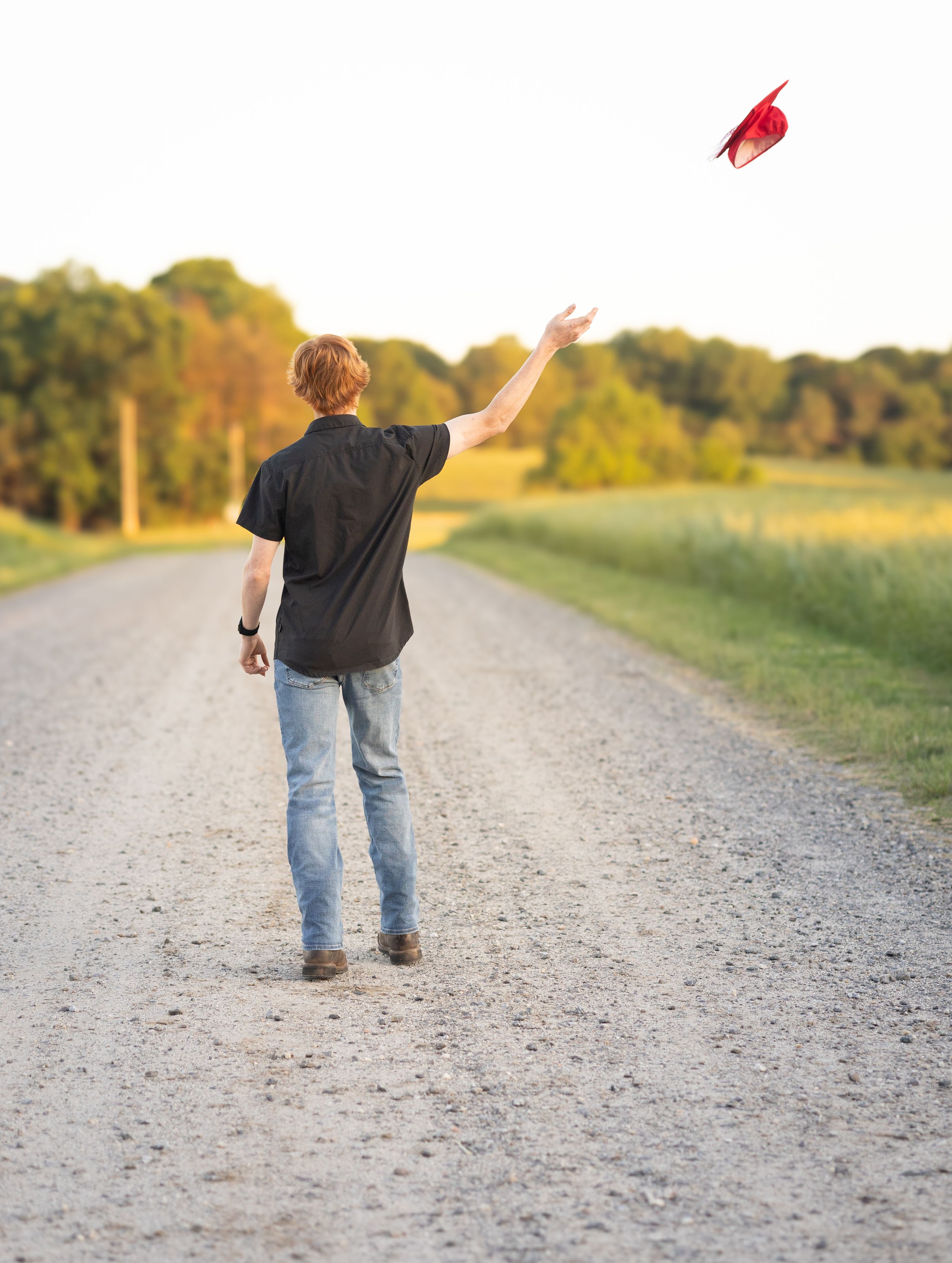 A child walking on a gravel path throws a red balloon into the sunny autumn sky.