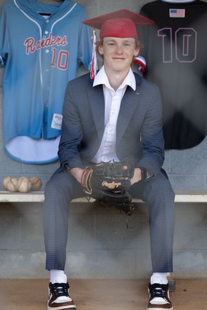 A close-up view of black and white oxford shoes worn with a grey suit in a baseball dugout setting.