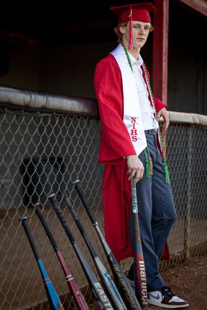 A row of colorful baseball bats lined up against a chain link fence with someone wearing a red jacket nearby.