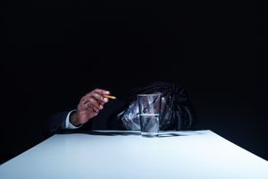 A dark silhouette of a person holding a flashlight beam against a black background.