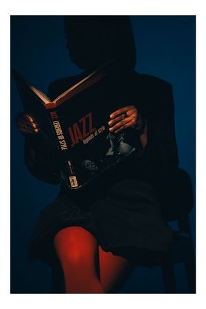 A silhouetted figure reading a book titled "Jazz" against a dark background with dramatic red lighting.