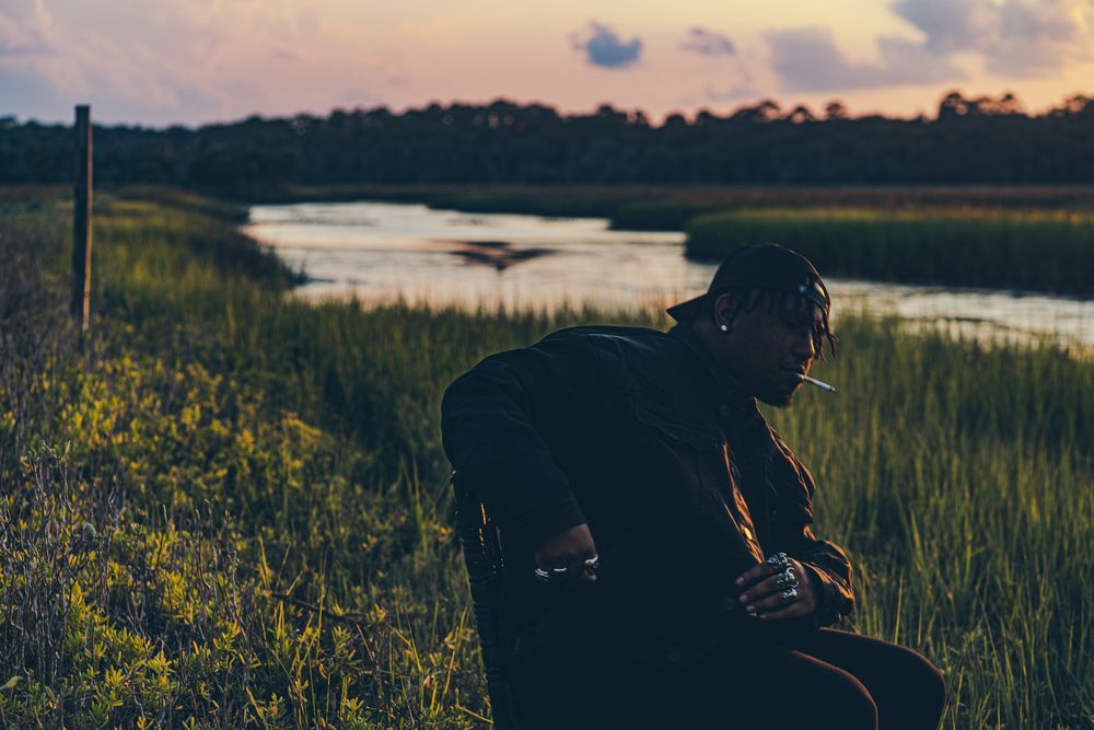 A scenic sunset view over coastal marshlands with tall grass and winding waterways in golden evening light.
