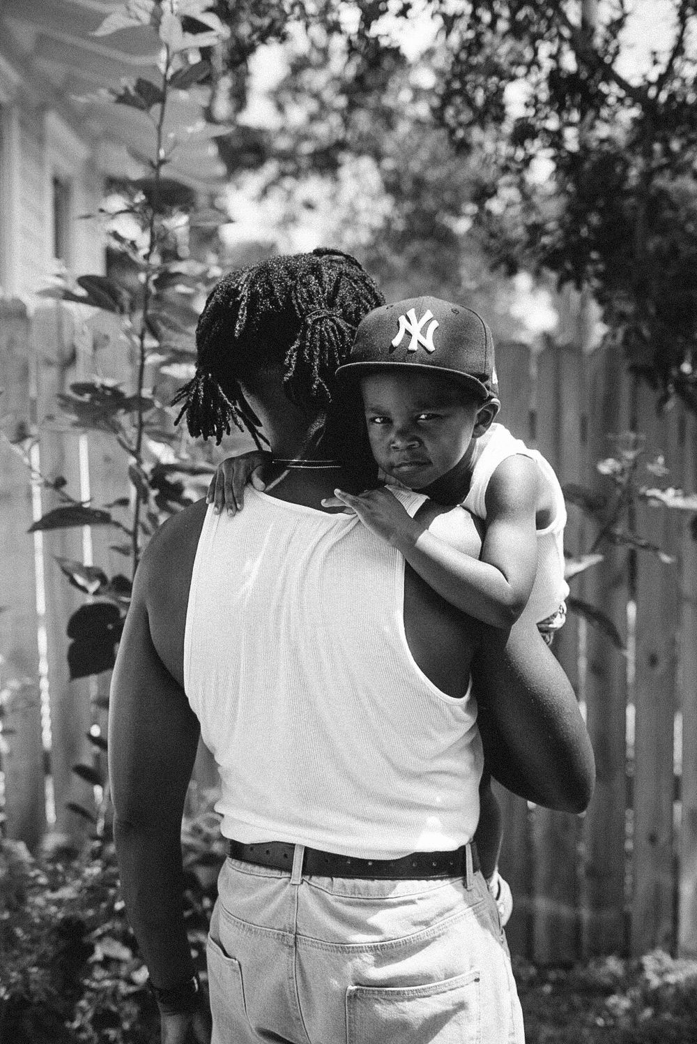 A sequence of black and white photographs showing someone wearing a white tank top and NY Yankees baseball cap.