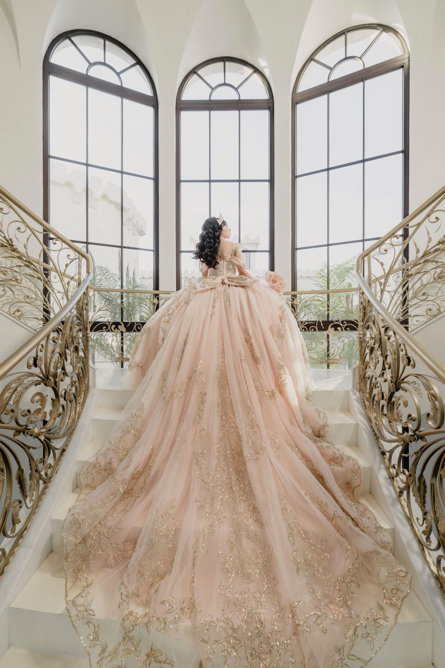 Stunning pink princess gown with sparkly tulle skirt displayed against large arched windows and ornate gold railings.