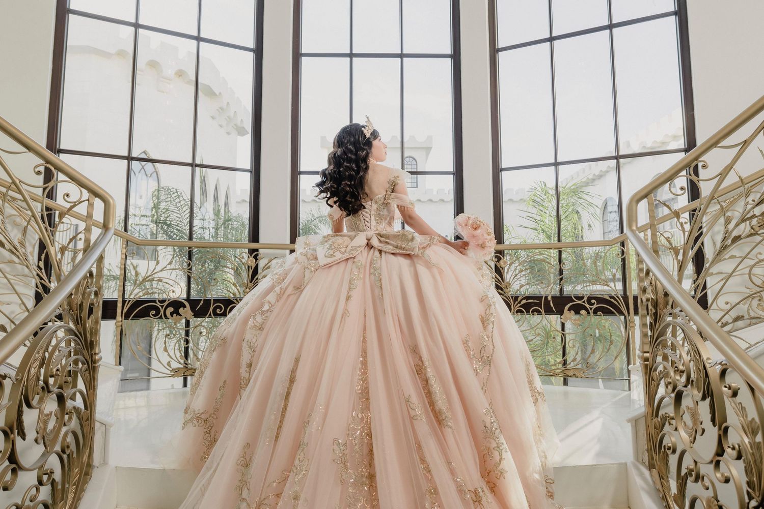 Elegant ballgown with champagne tulle and lace details photographed in a grand conservatory with ornate glass windows.
