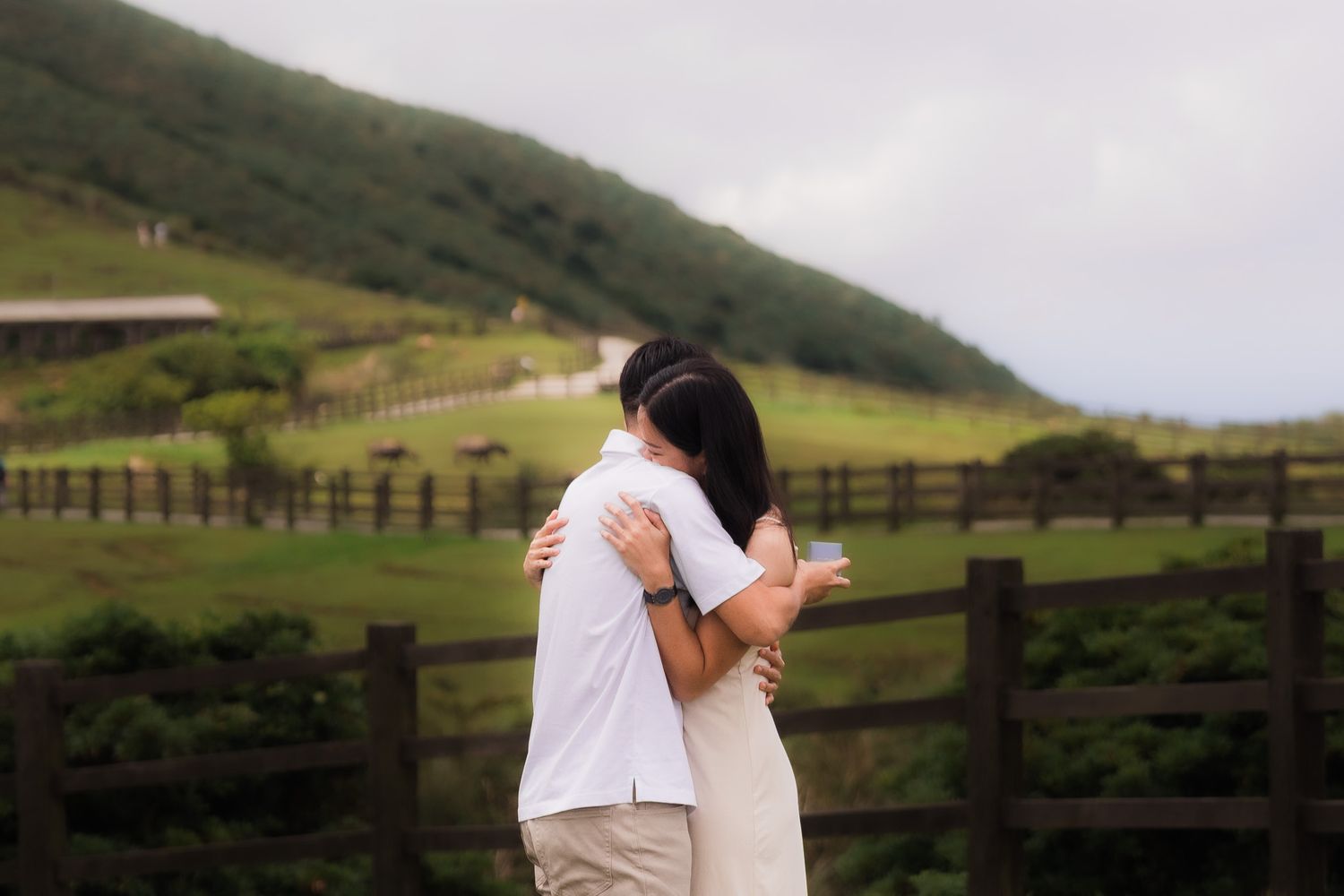 Couple walking hand in hand through lush green hills under cloudy skies in Hawaii.