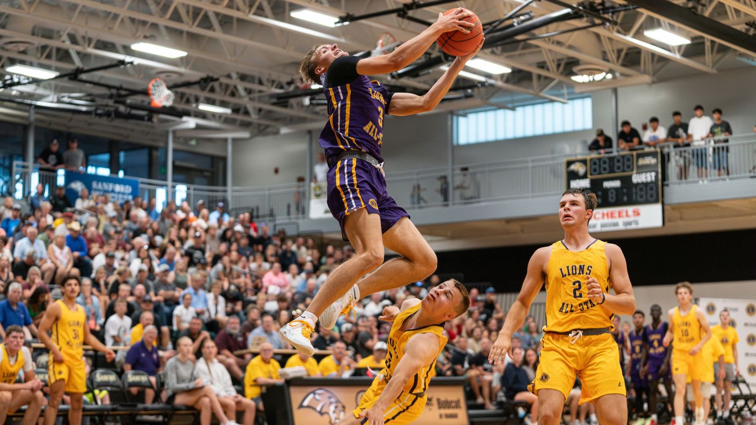 Basketball players compete in an intense game with yellow and blue uniformed teams on the court during a match.