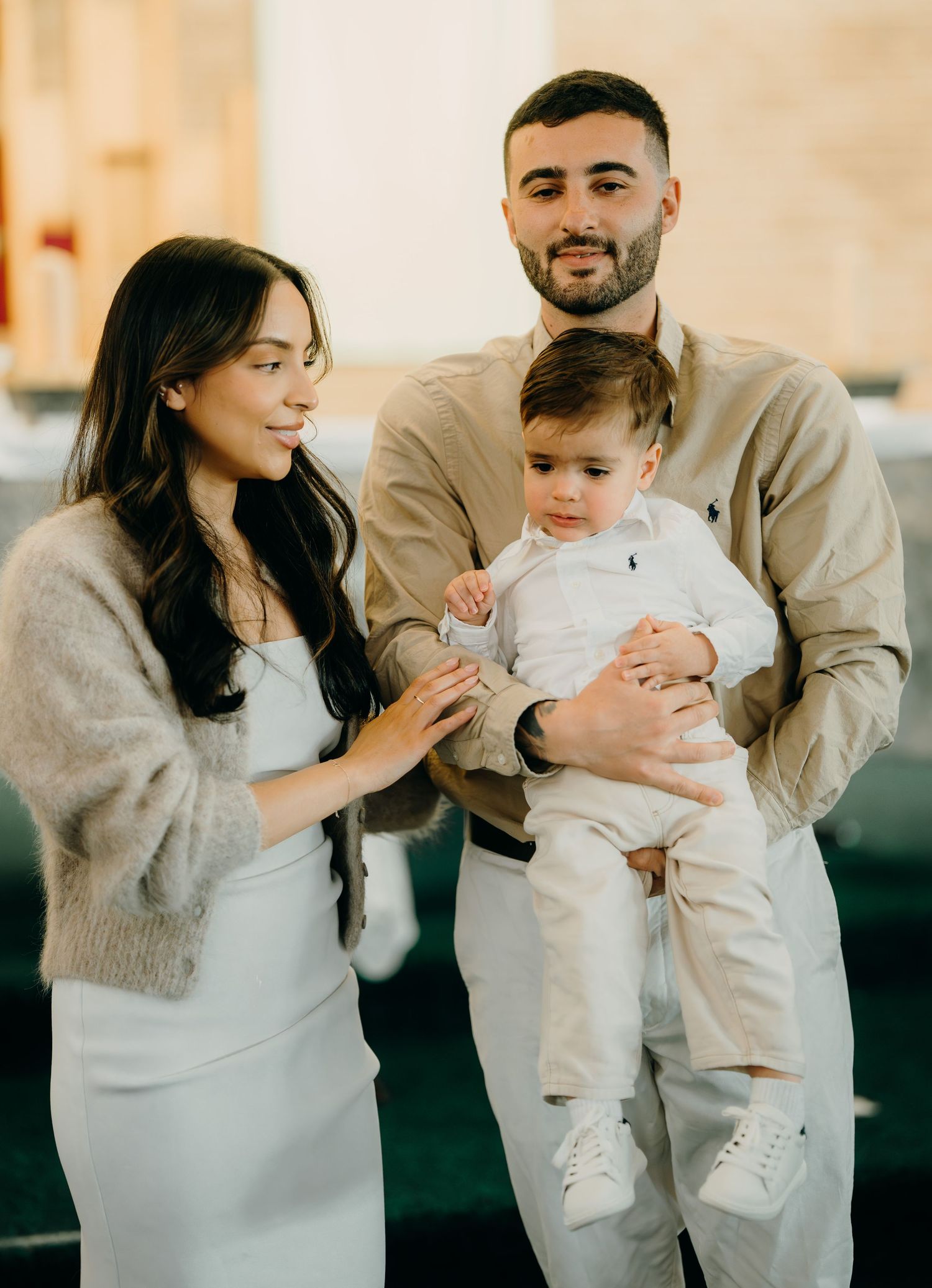 A couple in neutral-toned outfits plays and dances with their baby in three sequential shots on a light background.