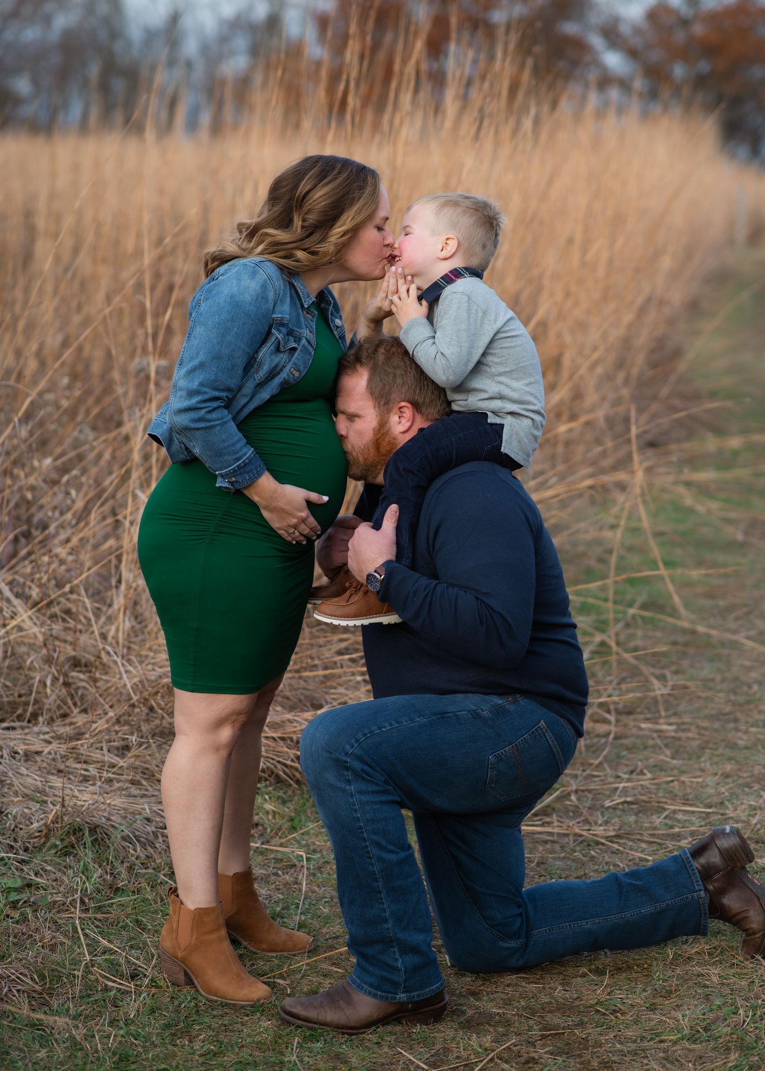 A tender family moment captured in tall golden grass during autumn with a green dress and denim clothing.