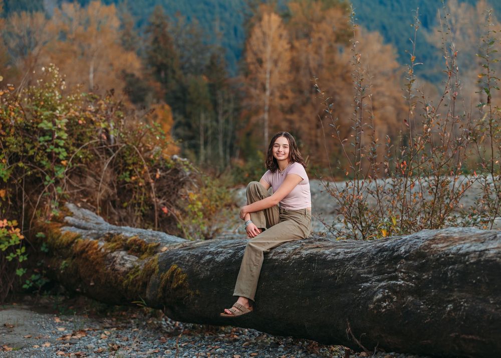 People sitting and posing on large fallen tree trunk with mountain backdrop.