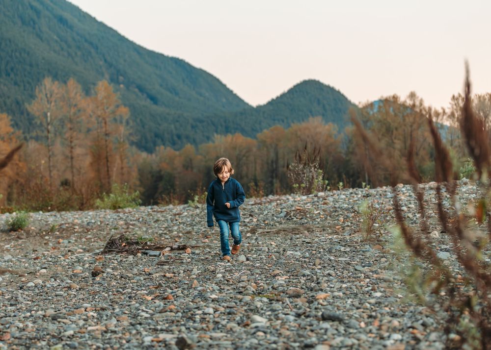 Rocky riverbed landscape with mountains and autumn trees in background.