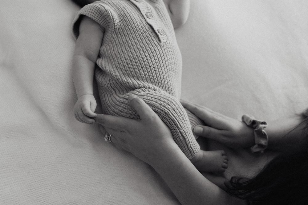 Close-up view of a baby wearing a soft gray ribbed onesie while resting on white bedding.