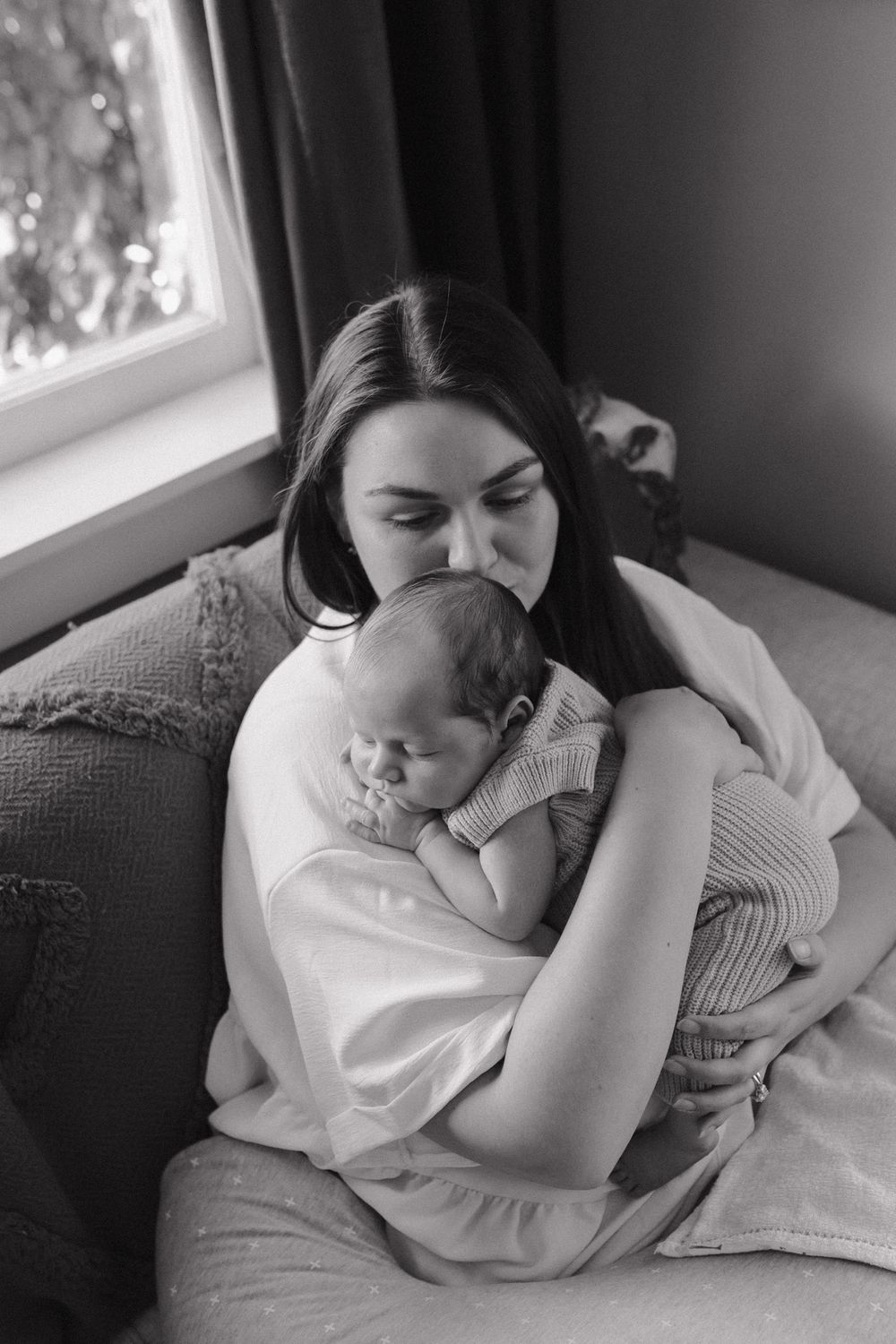 A black and white photo series showing tender moments of a mother and baby resting together on a couch.