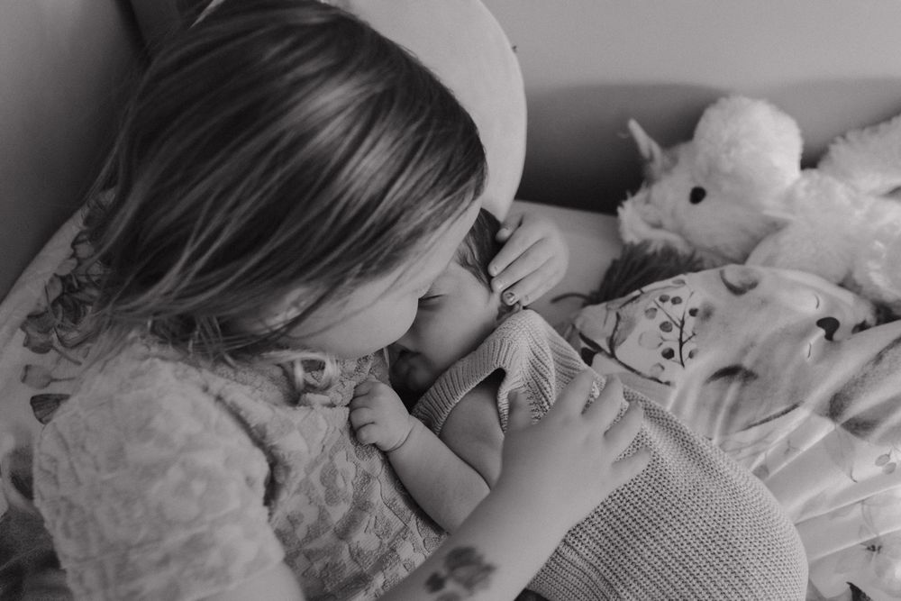 A child in pajamas lying in bed gives a goodnight kiss to a stuffed animal in this black and white photo.