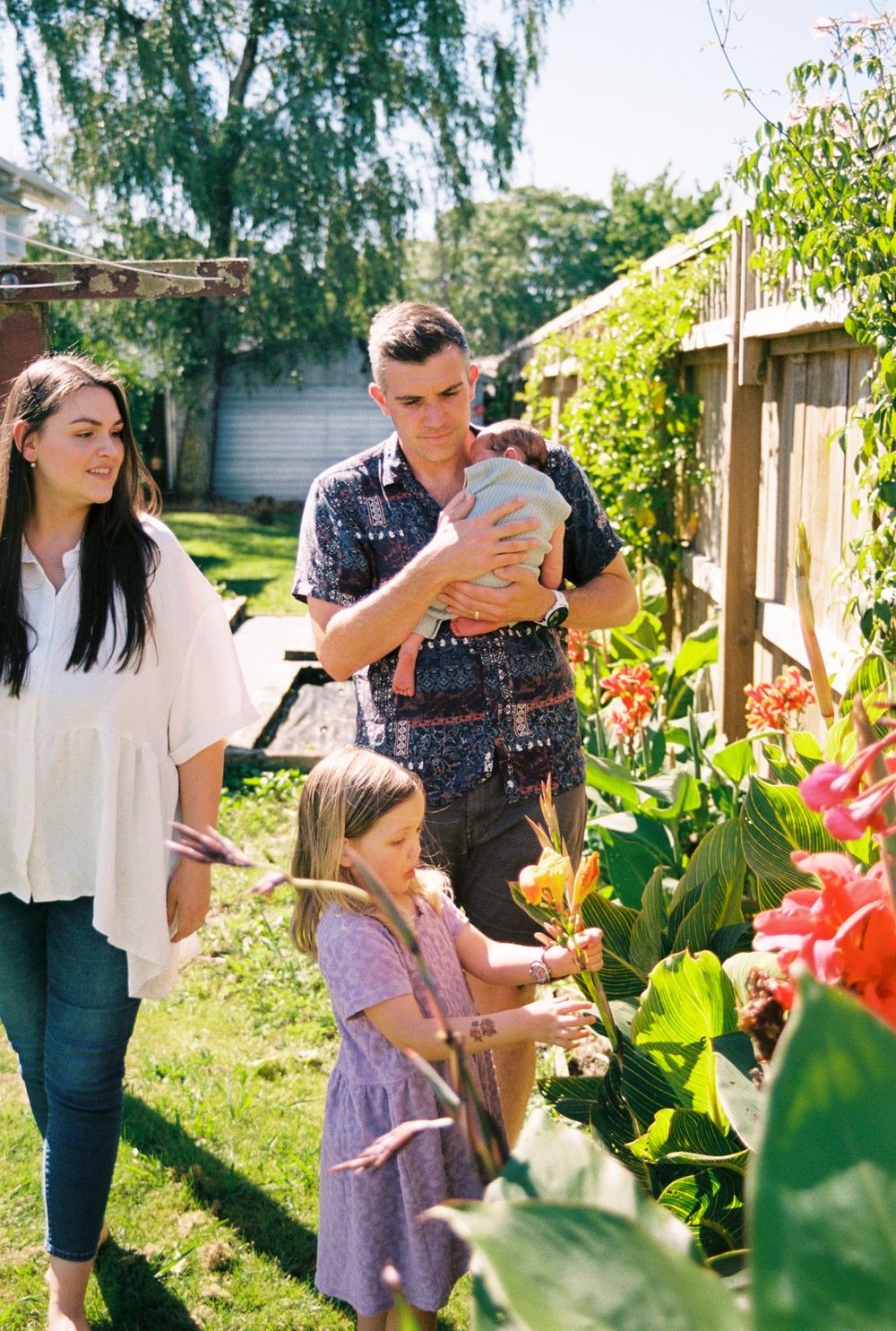 Family enjoying a playful moment together in a backyard garden with blooming flowers and greenery.