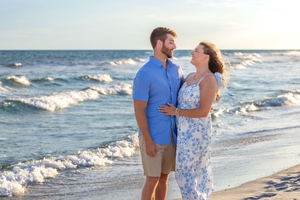 A couple shares a romantic moment together while walking on a beach at sunset with ocean waves in the background.