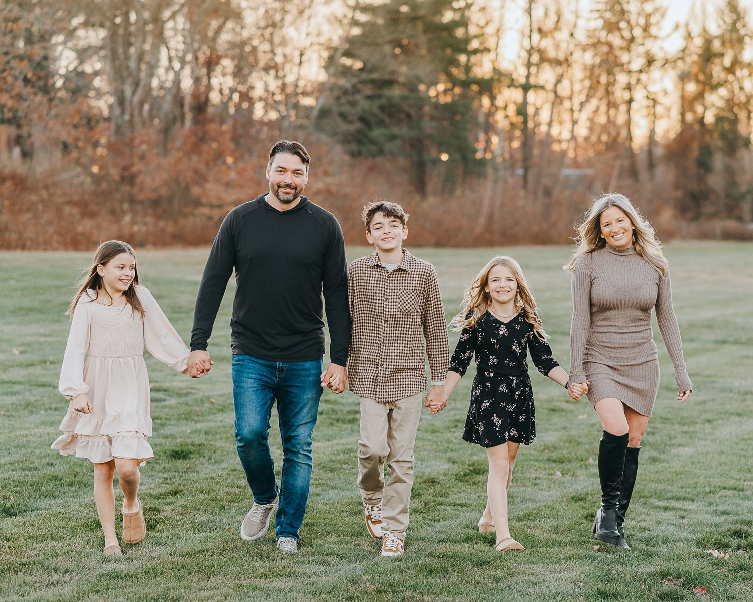 A group of people walking together across a grassy field during golden hour at sunset.