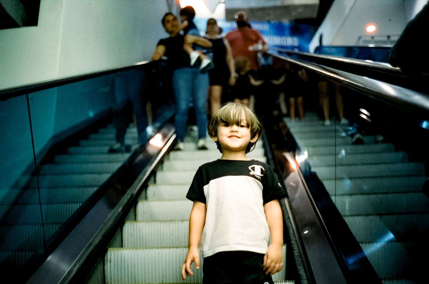 Person on escalator entrance inside modern metro station with blue lighting and stainless steel railings.