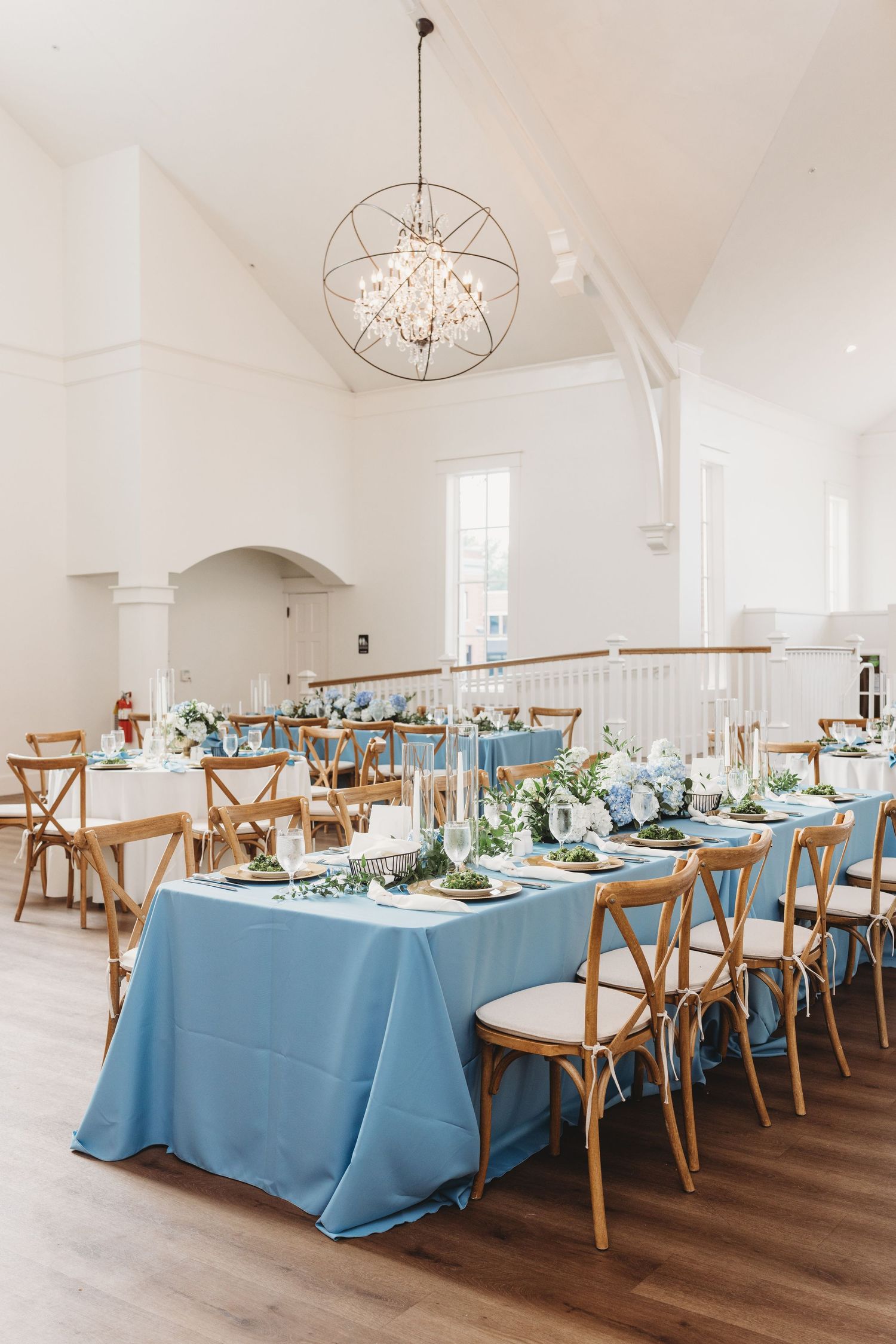 Elegant dining room setup with round table, cross-back chairs, ornate gold mirrors and pendant lights in white arched space.