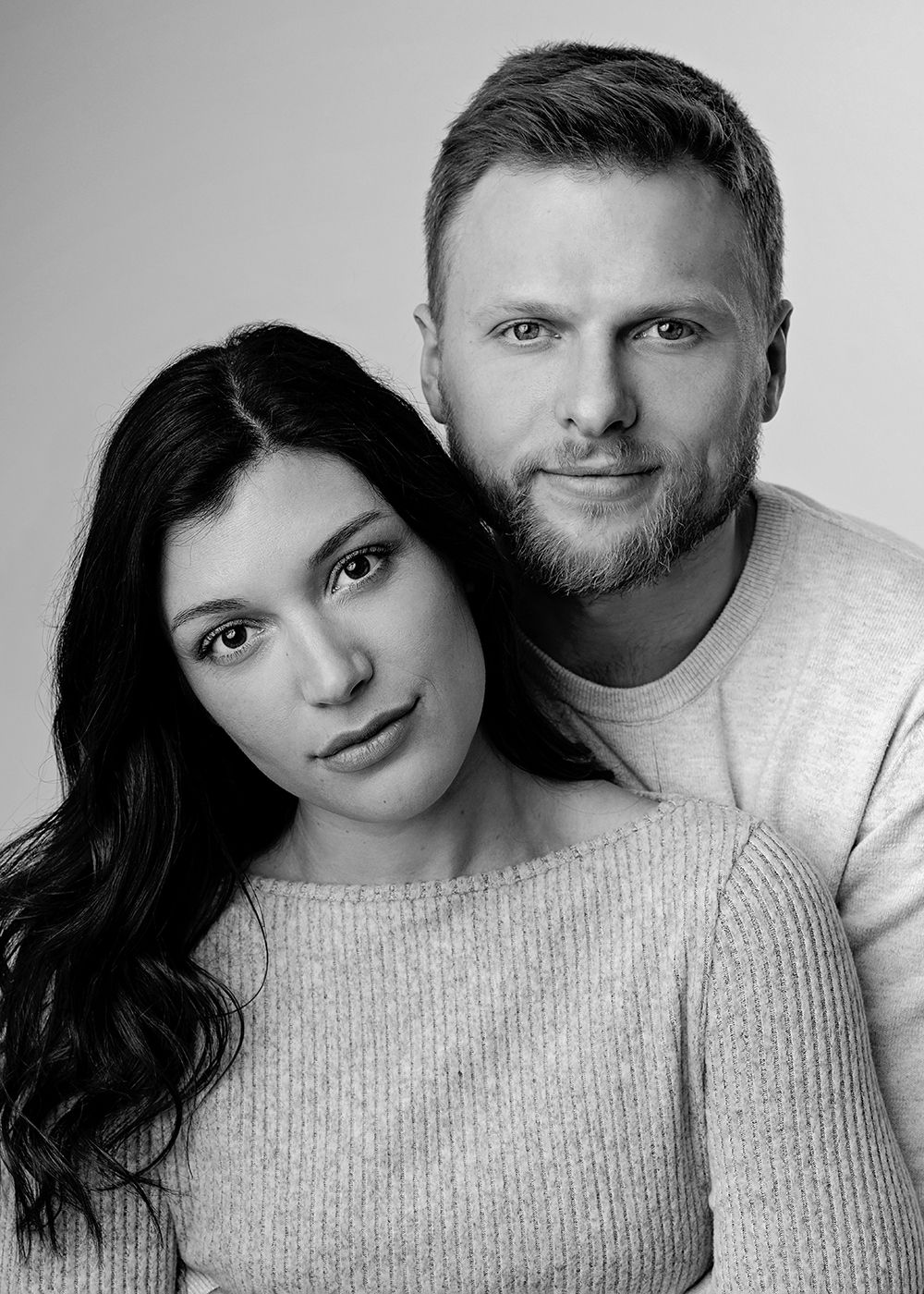 Black and white portrait of a couple in matching light sweaters posing together against a simple background.