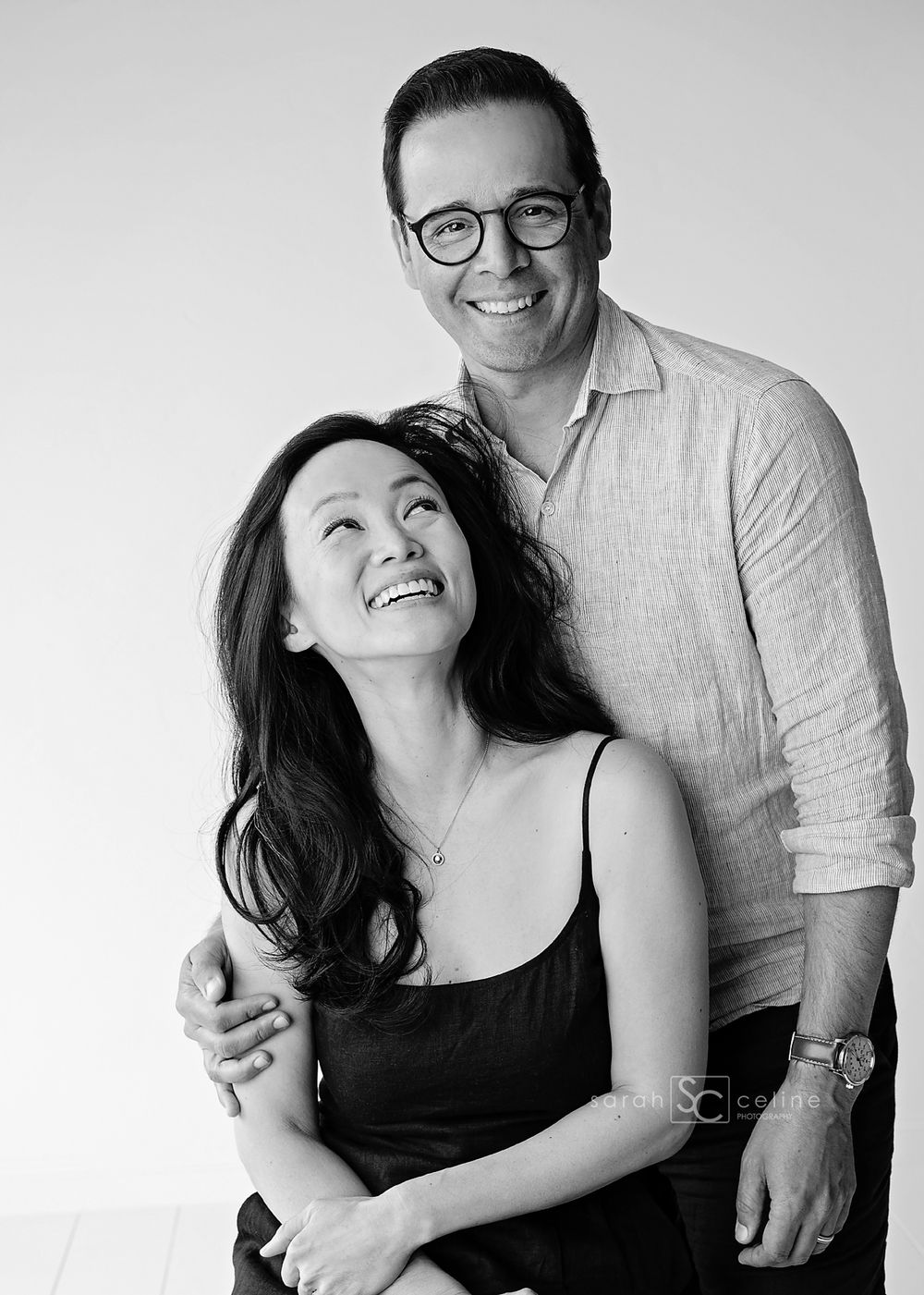A black and white portrait of a happy couple embracing and laughing together while dressed casually.