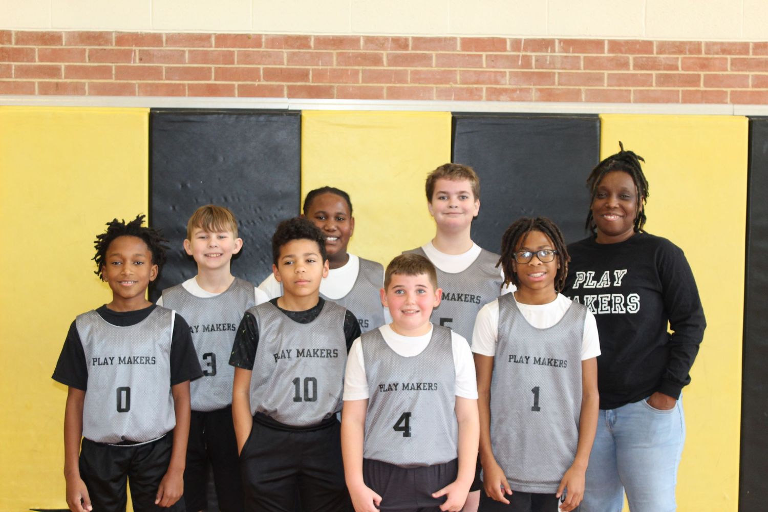 Youth basketball team poses together wearing matching gray jerseys in front of yellow wall.