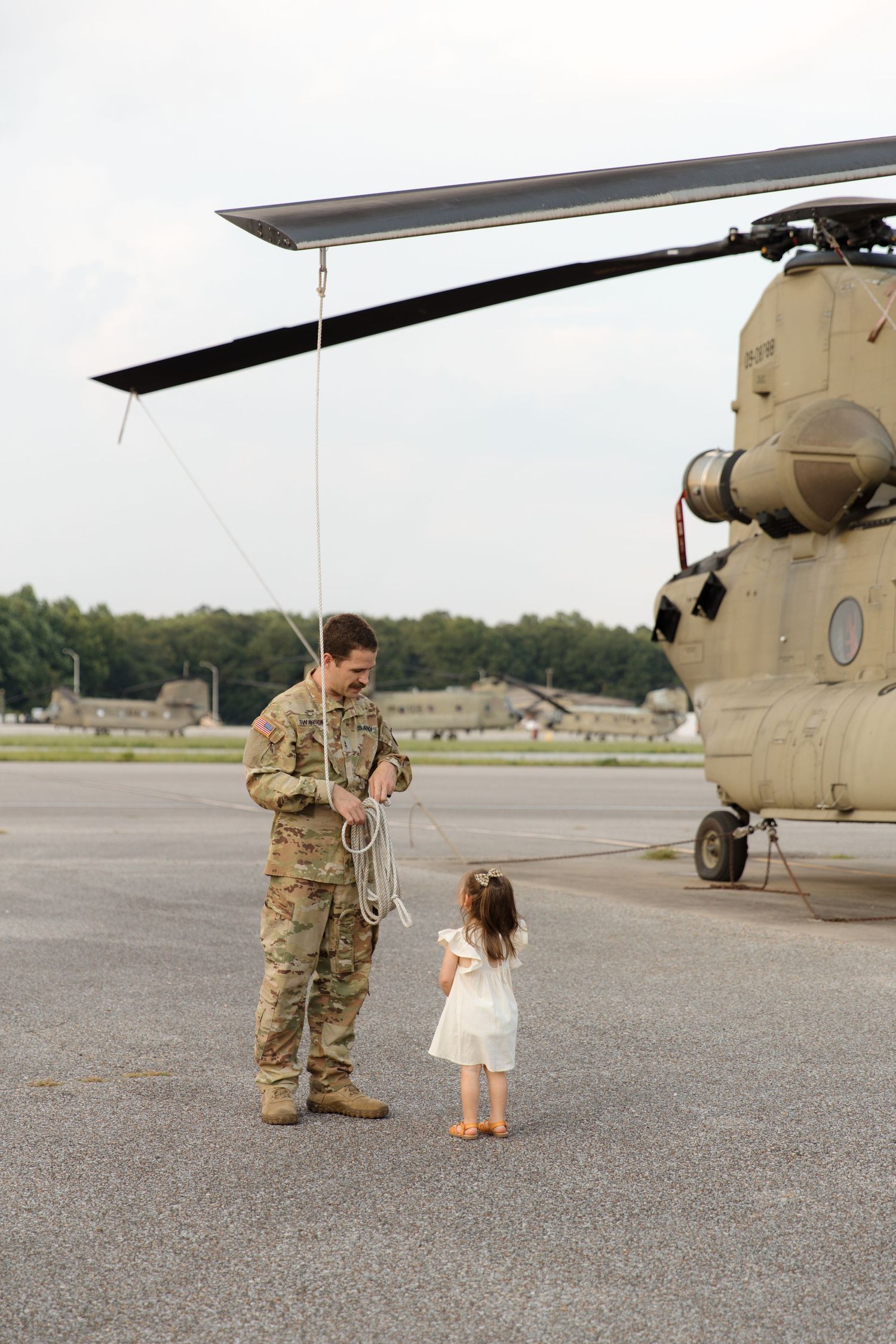 A service member in uniform stands with a small child next to a military helicopter.