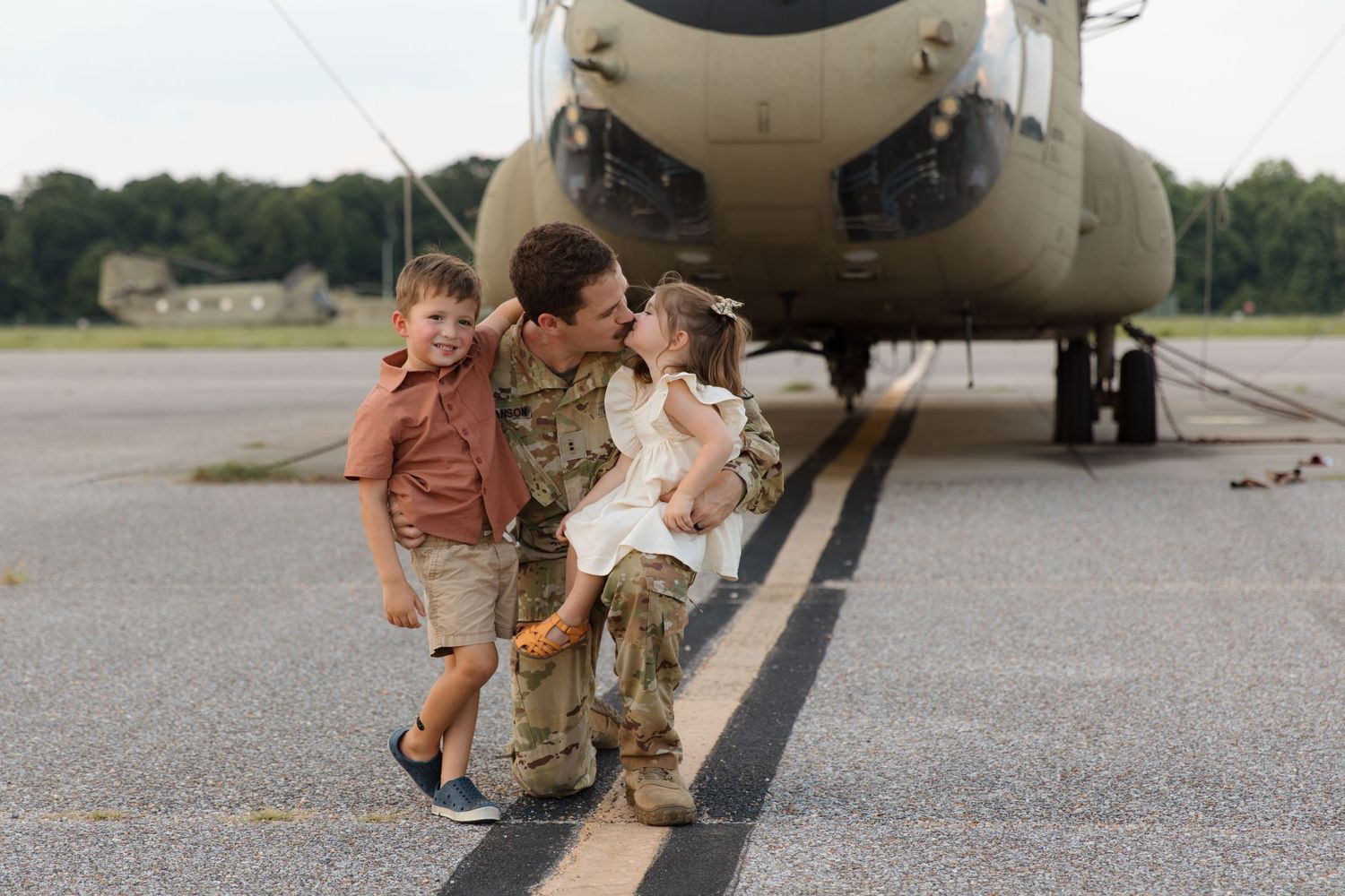 A heartwarming family moment captured in front of a military helicopter on an airfield.