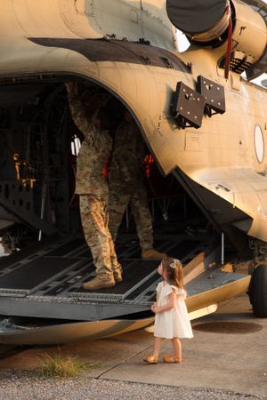 Military helicopter ramp view with service member and small figure in white dress.