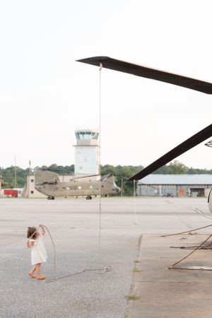 Distant view of helicopter on airfield with small figure walking nearby.
