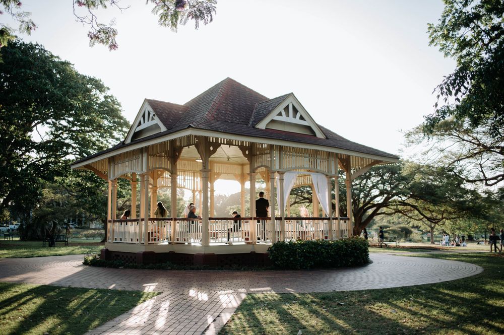 A charming white Victorian-style gazebo photographed in golden hour light surrounded by lush trees.