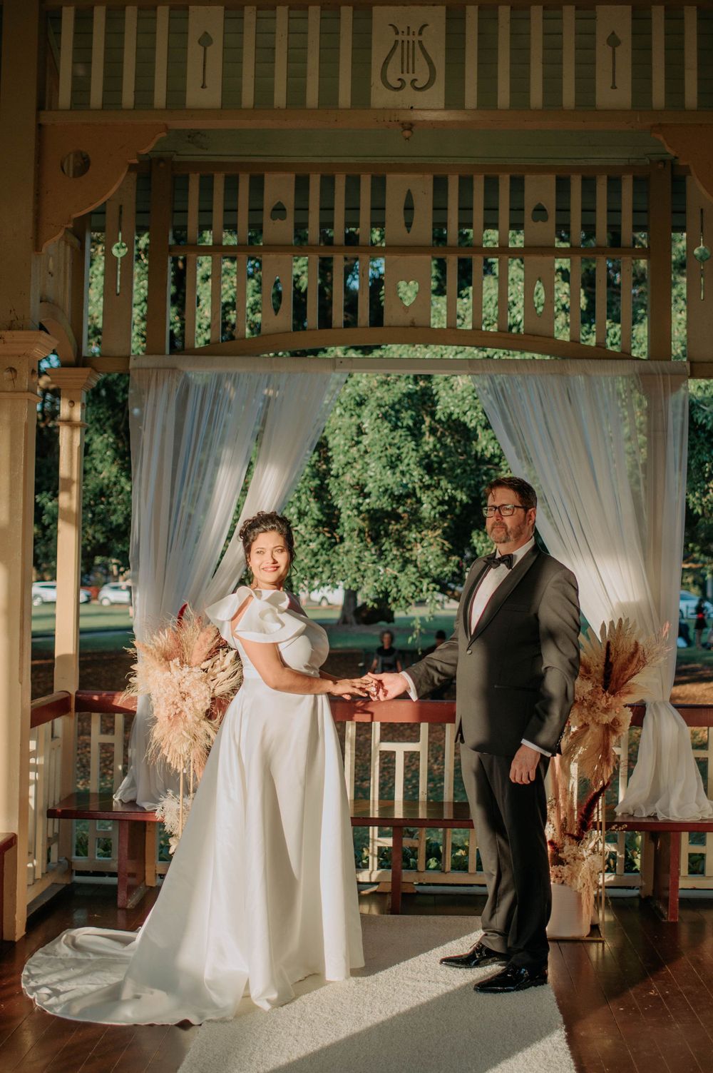 Couple stands in decorated gazebo with dried floral arrangements and delicate drapery.