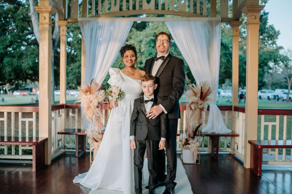 A wedding portrait in a decorated gazebo with white curtains and pampas grass arrangements.
