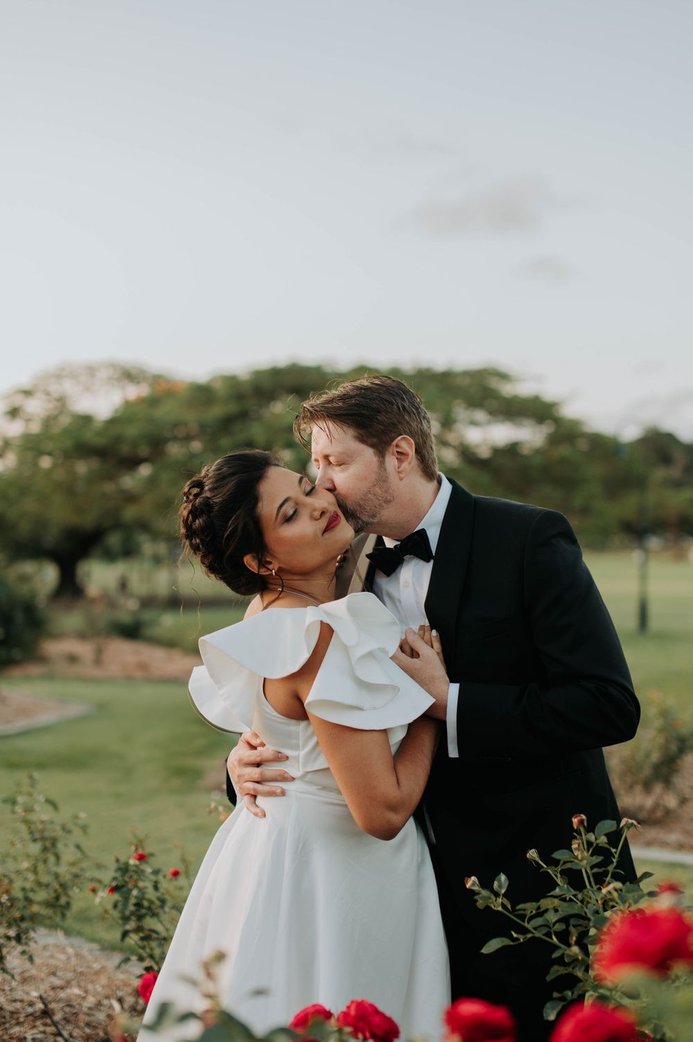 Intimate moment between newlyweds among blooming red flowers in garden setting.