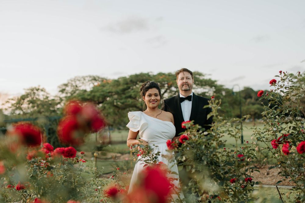 A wedding portrait in a garden with blooming red roses in the foreground.