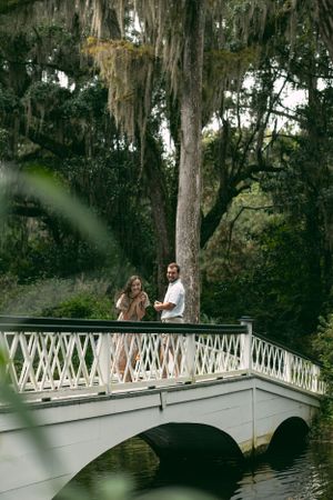 A couple standing on a white painted bridge in a southern garden with hanging moss.