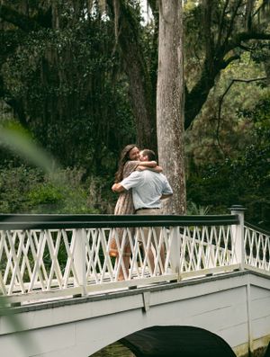 A couple embracing on a white bridge surrounded by moss-draped trees.