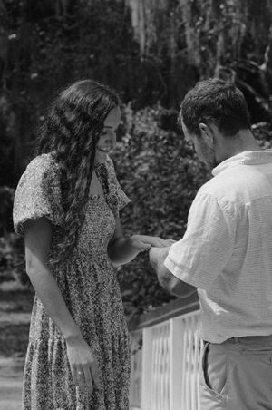 A couple exchanging rings during a proposal on a white bridge in a garden.