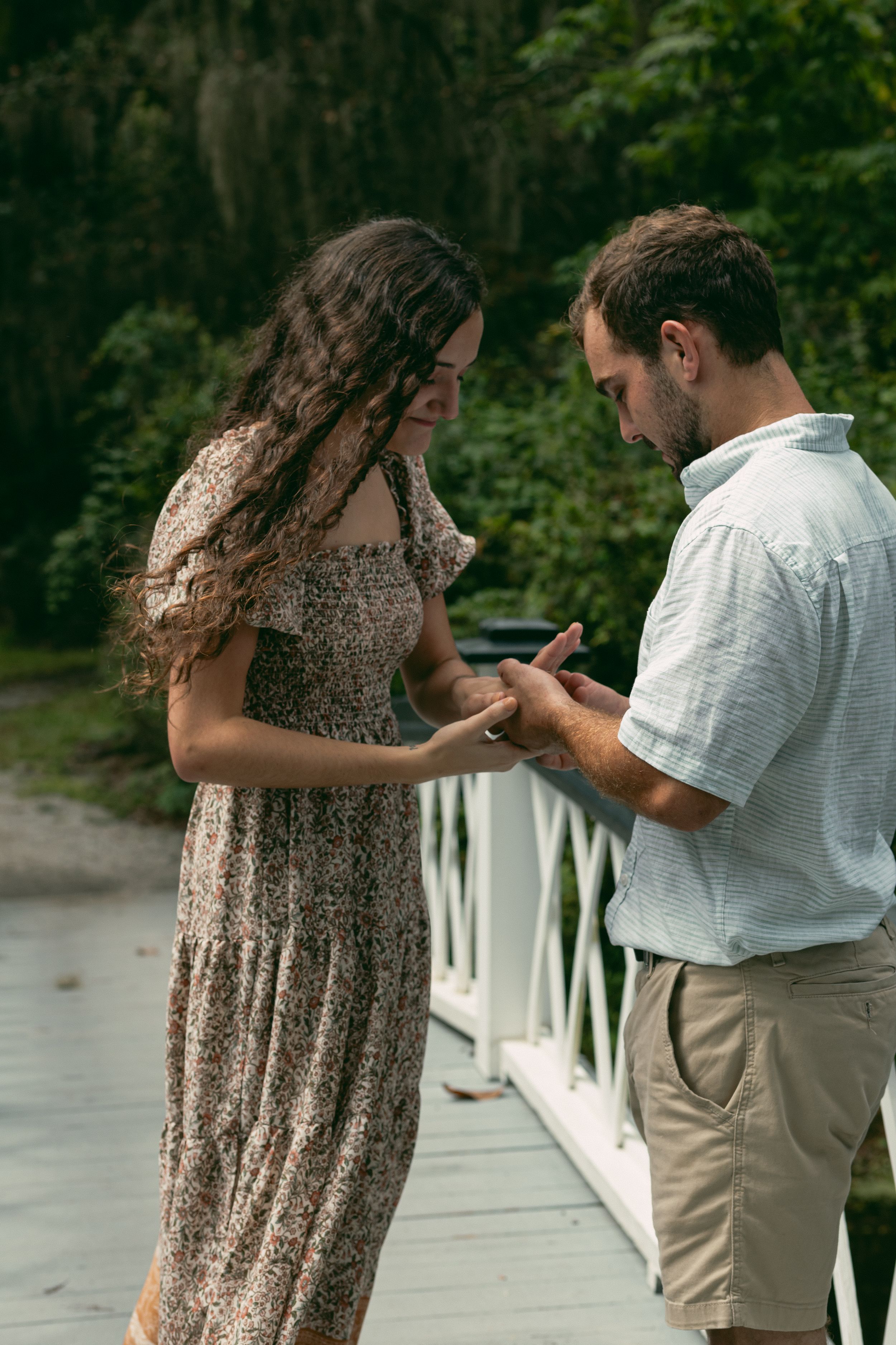 A couple shares an intimate moment on a white bridge surrounded by trees.