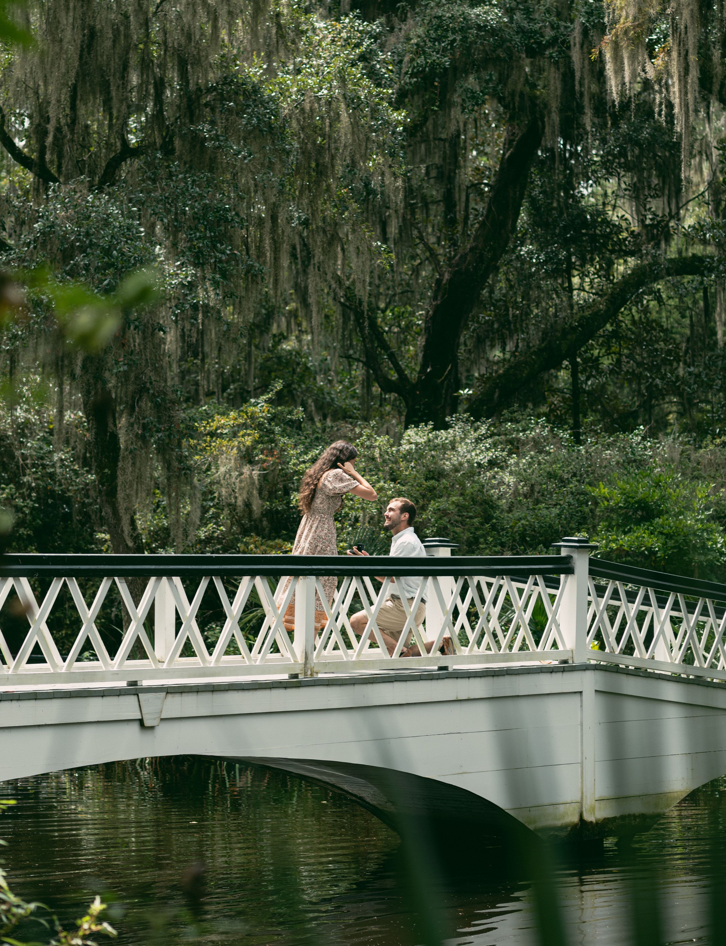 A couple sharing a romantic moment on a white bridge in a southern garden with Spanish moss.