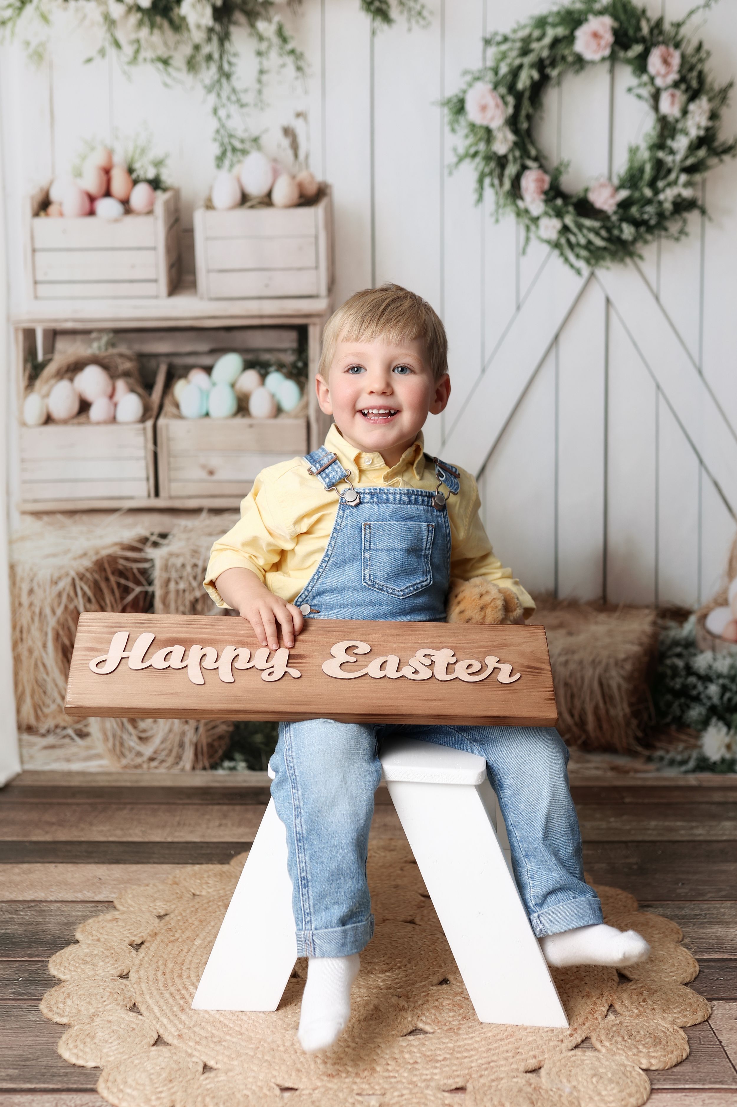 Sweet Easter portrait setup with wooden decor, floral wreath, rustic crates and bunny decorations against white barn door backdrop.